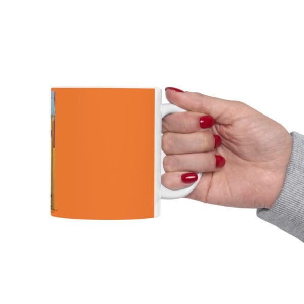 A hand holding a white mug with orange design.