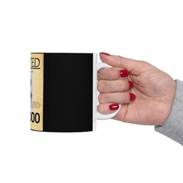 Hand holding a black mug with a wanted poster on it.