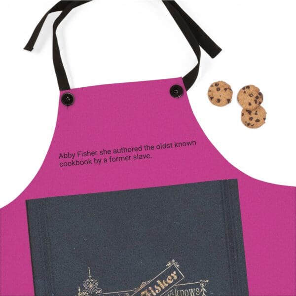 A pink apron with a black ribbon and two cookies